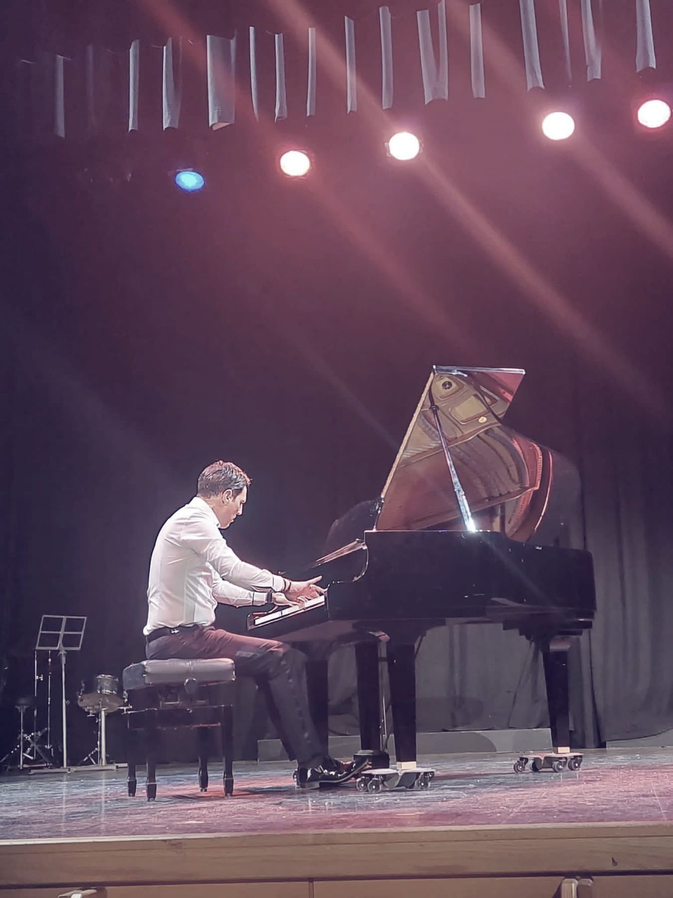 Sergio Cano Ortiz tocando un piano de cola en un escenario, bajo focos de colores.